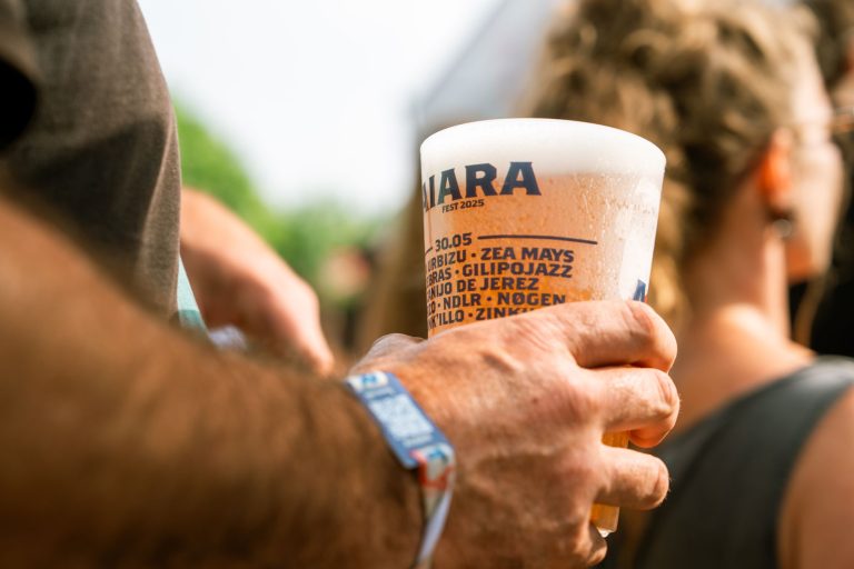 Osoba trzyma kubek piwa na plenerowym festiwalu muzycznym
